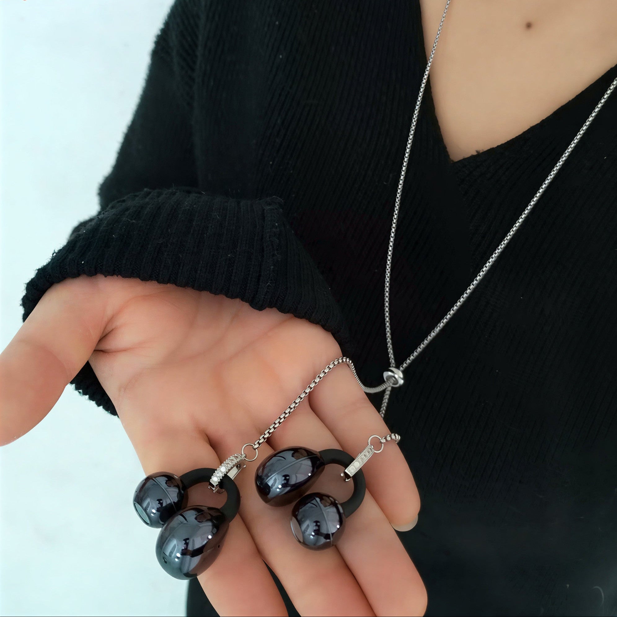 Person holding two black pendant necklaces with a plain background