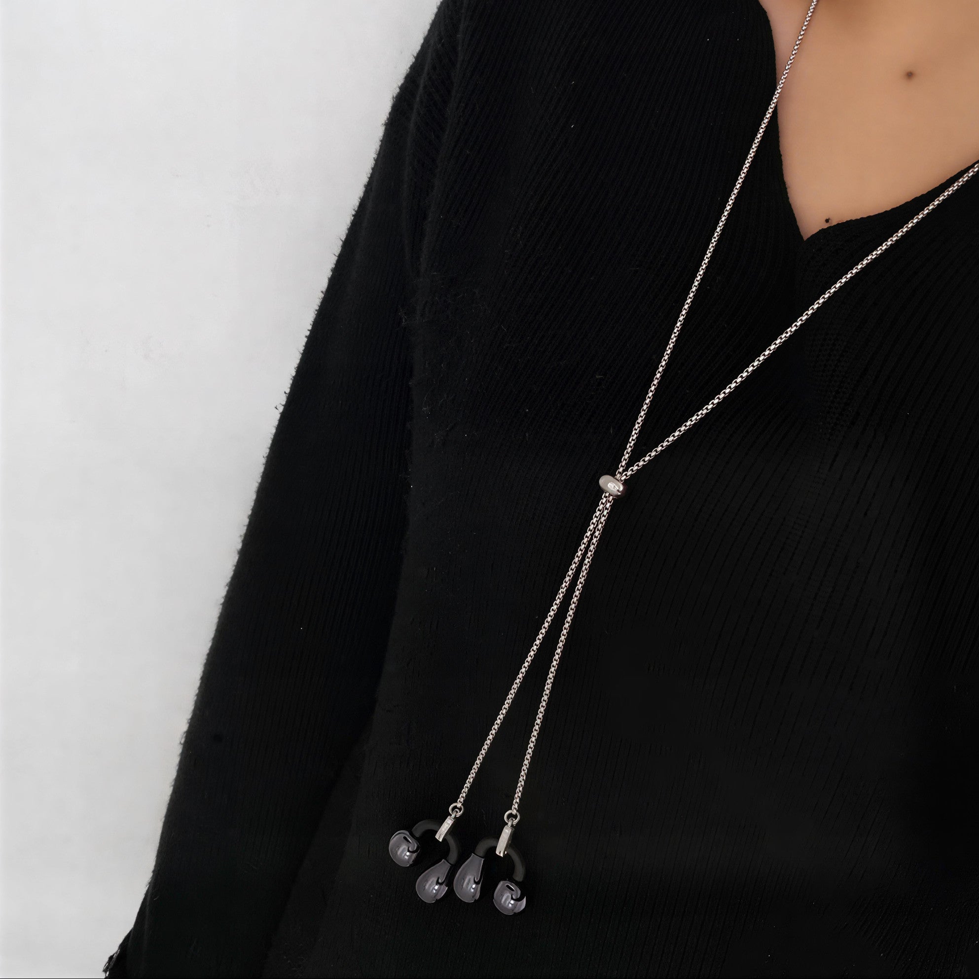 Long necklace with pendant on a person wearing a black outfit against a white background